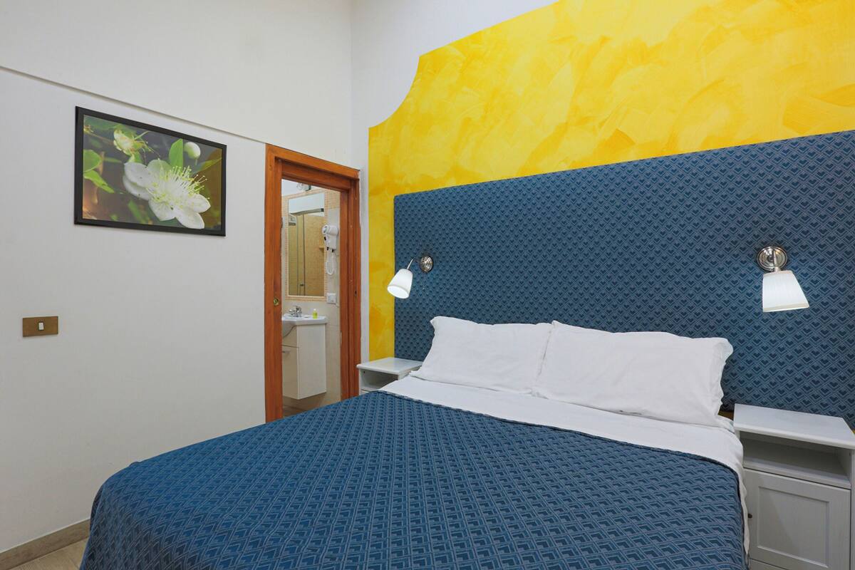 A neatly made bed with a blue patterned bedspread, a white pillow, and two bedside lamps.