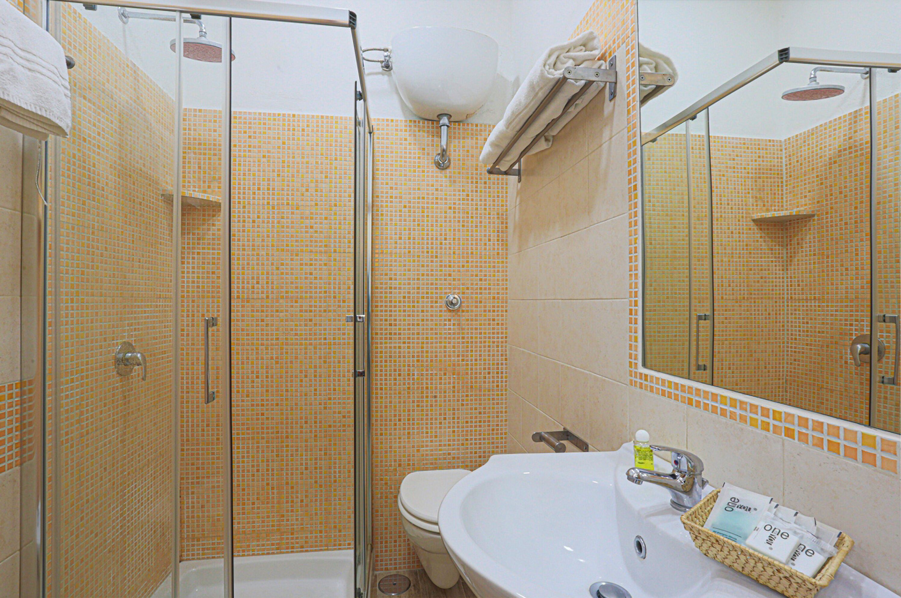 Een badkamer met een douchecabine van glas, een wit wastafelmeubel en een betegelde muur.