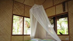 Une chambre avec un lit, une fenêtre donnant sur un paysage verdoyant et une moustiquaire au-dessus du lit.