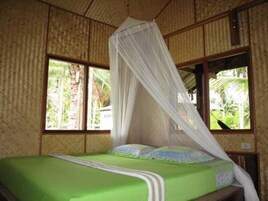 Una habitación con cama, ventana y vistas a la vegetación, además de mosquitero sobre la cama.