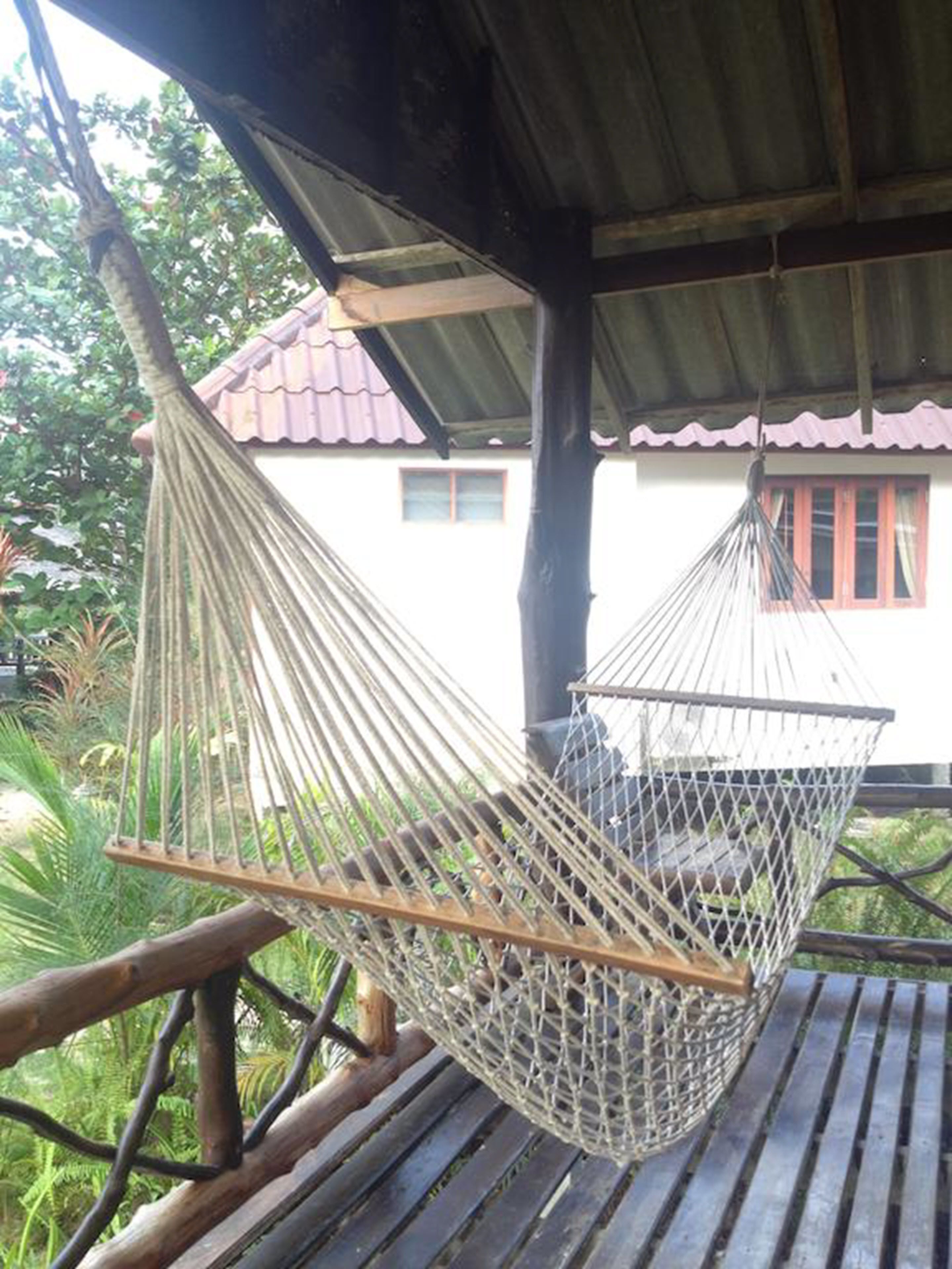 A hammock suspended between wooden beams, with a view of a building in the background.