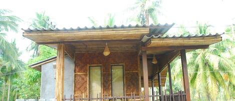 A wooden house with a balcony, two windows, and a corrugated metal roof.