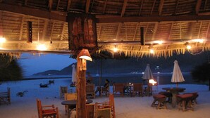 Un espace extérieur aménagé avec des tables et des chaises, un toit de chaume et une vue sur la plage et la mer.