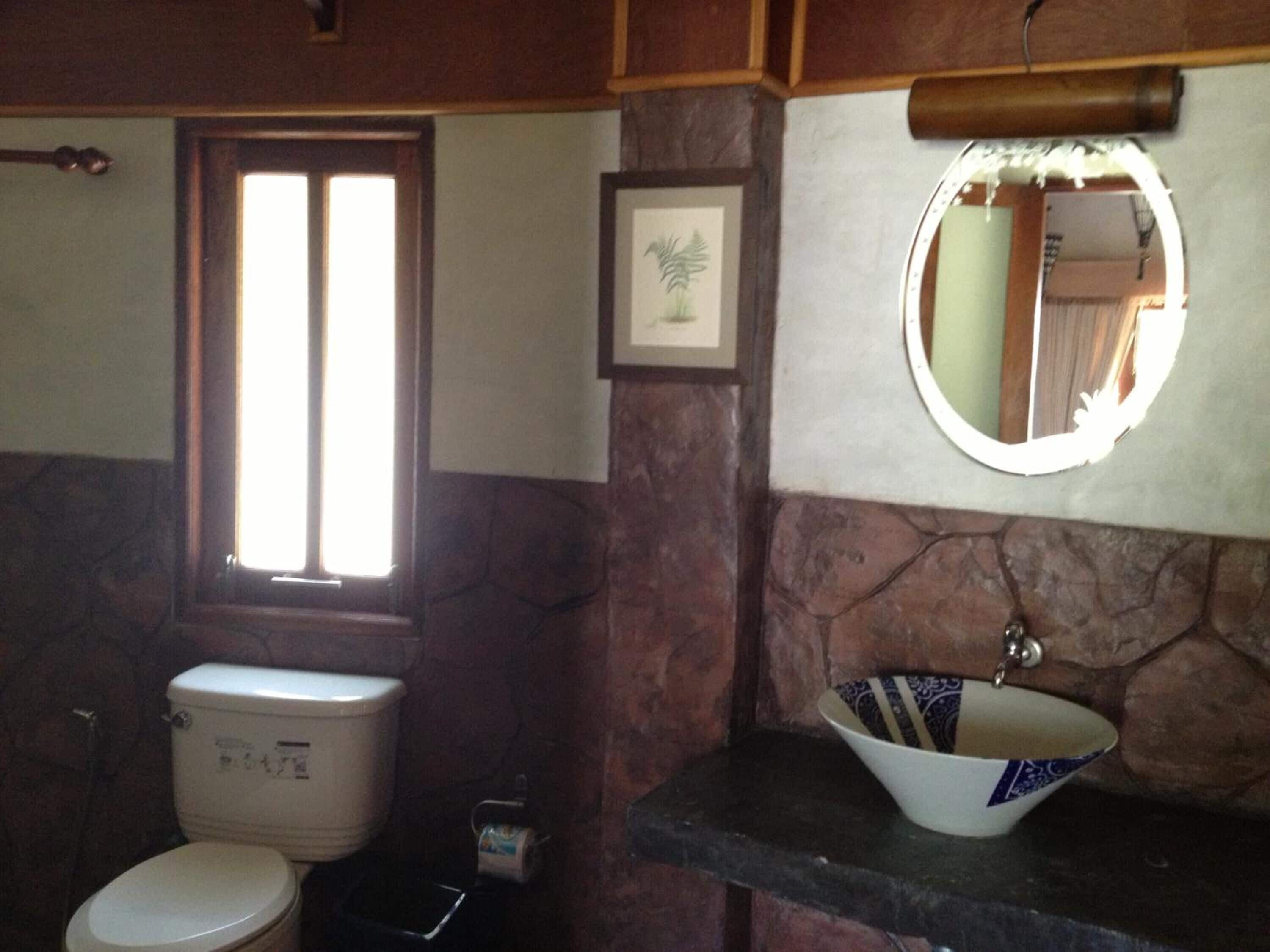 A bathroom with a toilet, a sink with a bowl, a framed picture on the wall, and a window.