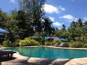 Una piscina al aire libre, sombrillas, sillones reclinables de piscina
