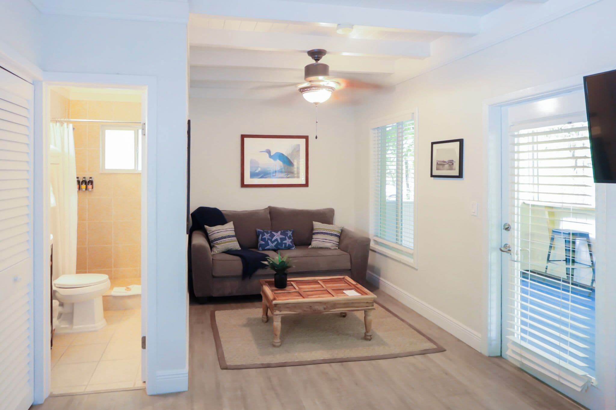 A living room with a ceiling fan, a sofa, a coffee table, and a door leading to a balcony.