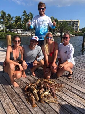 A group of people on a wooden dock with a pile of lobsters in front of them. - Coconut Palm Inn (Tavernier)