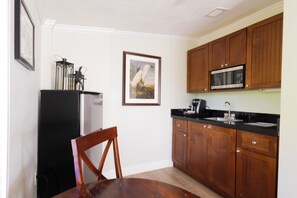 A kitchen with wooden cabinets, a black refrigerator, a microwave, and a dining table with chairs. - Coconut Palm Inn (Tavernier)