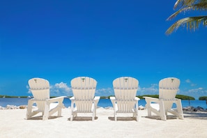 Four white Adirondack chairs facing a body of water with a clear sky. - Coconut Palm Inn (Tavernier)