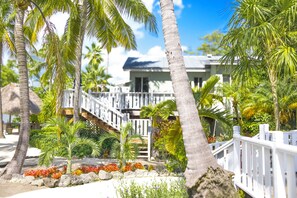 A beachfront property with a wooden staircase leading to a white balcony, surrounded by palm trees and tropical plants. - Coconut Palm Inn (Tavernier)
