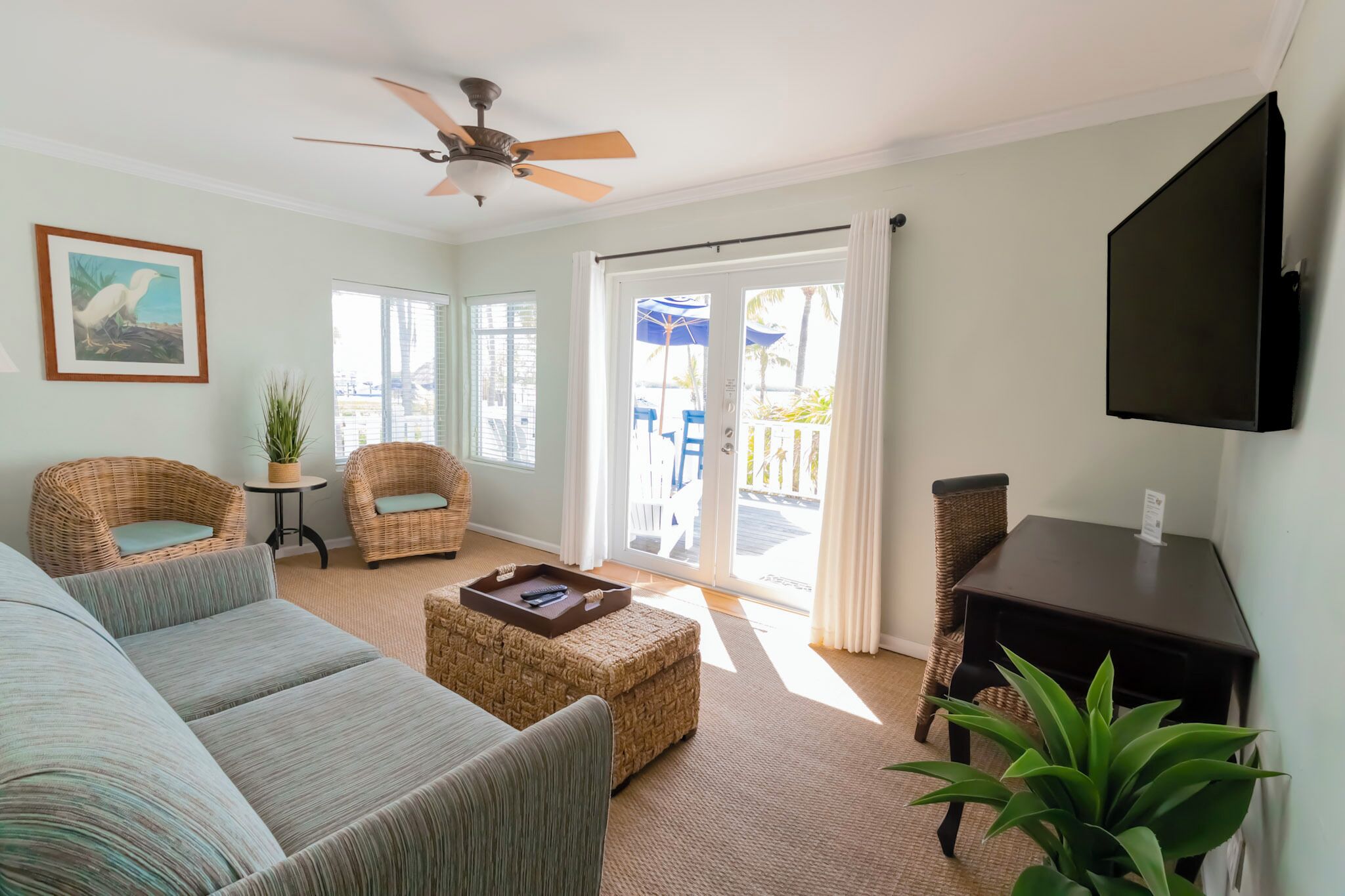 A living room with a sofa, two wicker chairs, a coffee table, a television, and a ceiling fan.