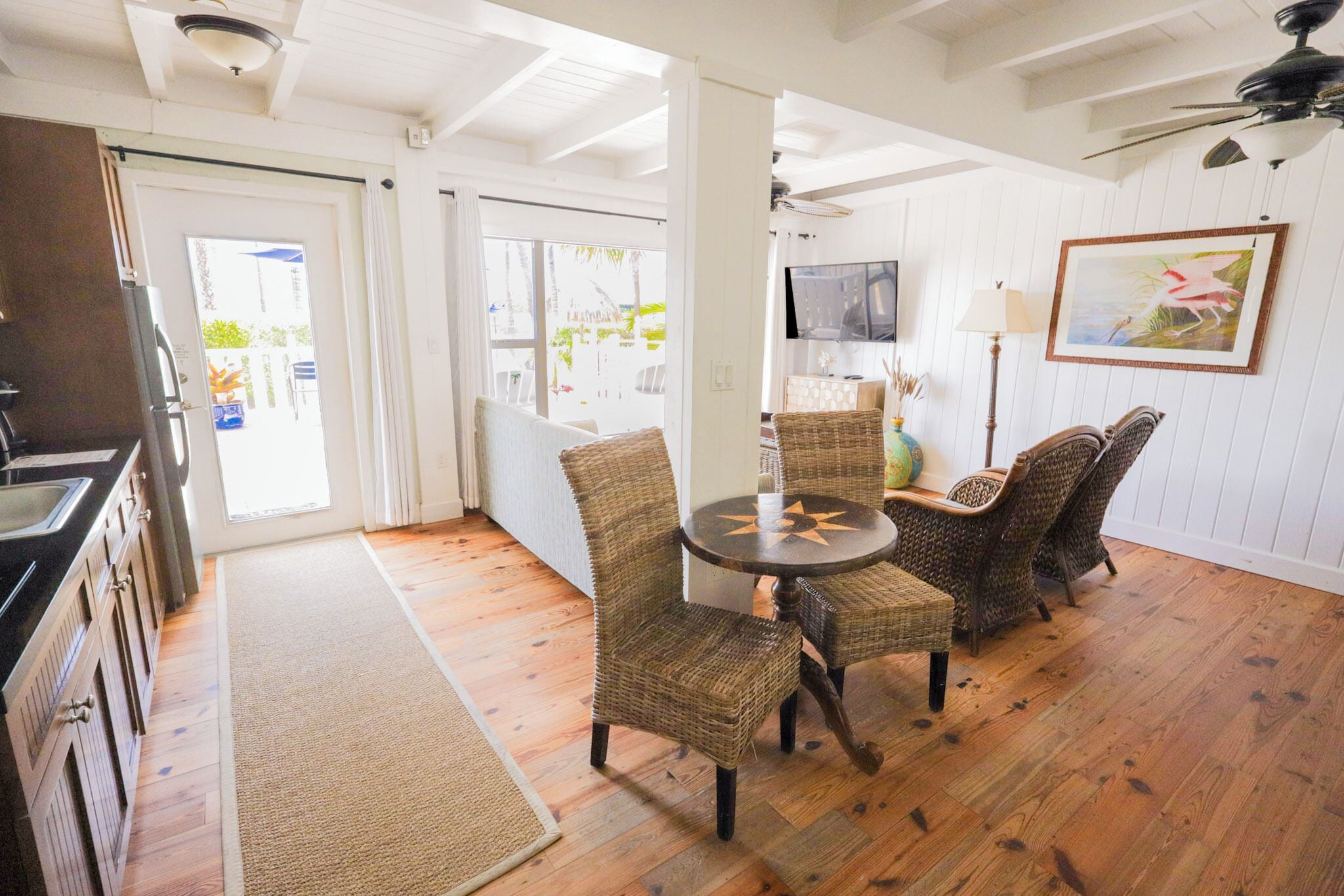 A room with a dining table and chairs, a kitchen area, and a television on the wall.