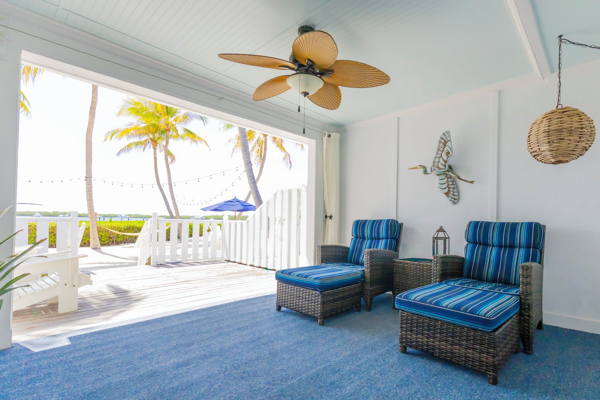 A room with wicker furniture, a ceiling fan, and a view of palm trees.