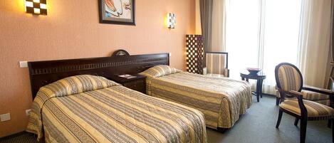 A hotel room with two beds, a desk, a chair, and a large window with curtains.