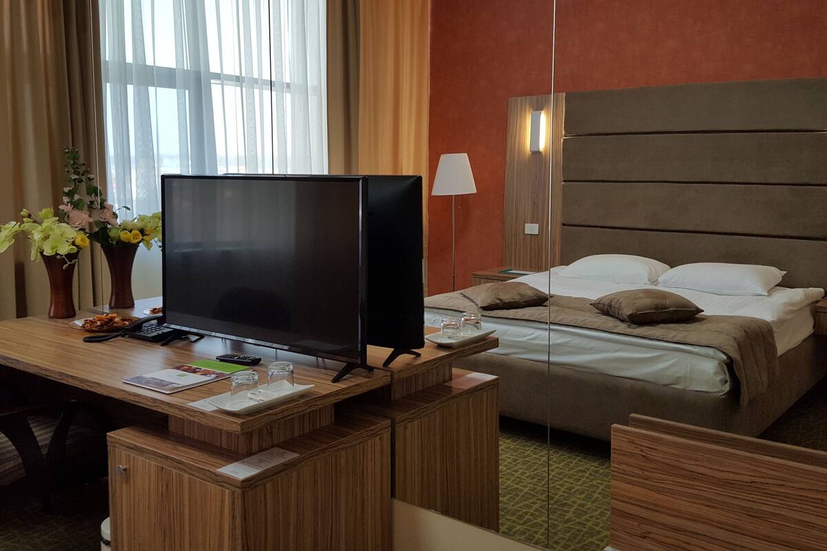 Ein Hotelzimmer mit einem Bett, einem Schreibtisch mit Fernseher, einer Lampe und einer Vase mit Blumen.