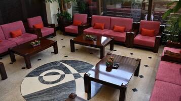 Un vestíbulo con sofás rojos, mesas de madera, piso estampado y plantas en macetas.