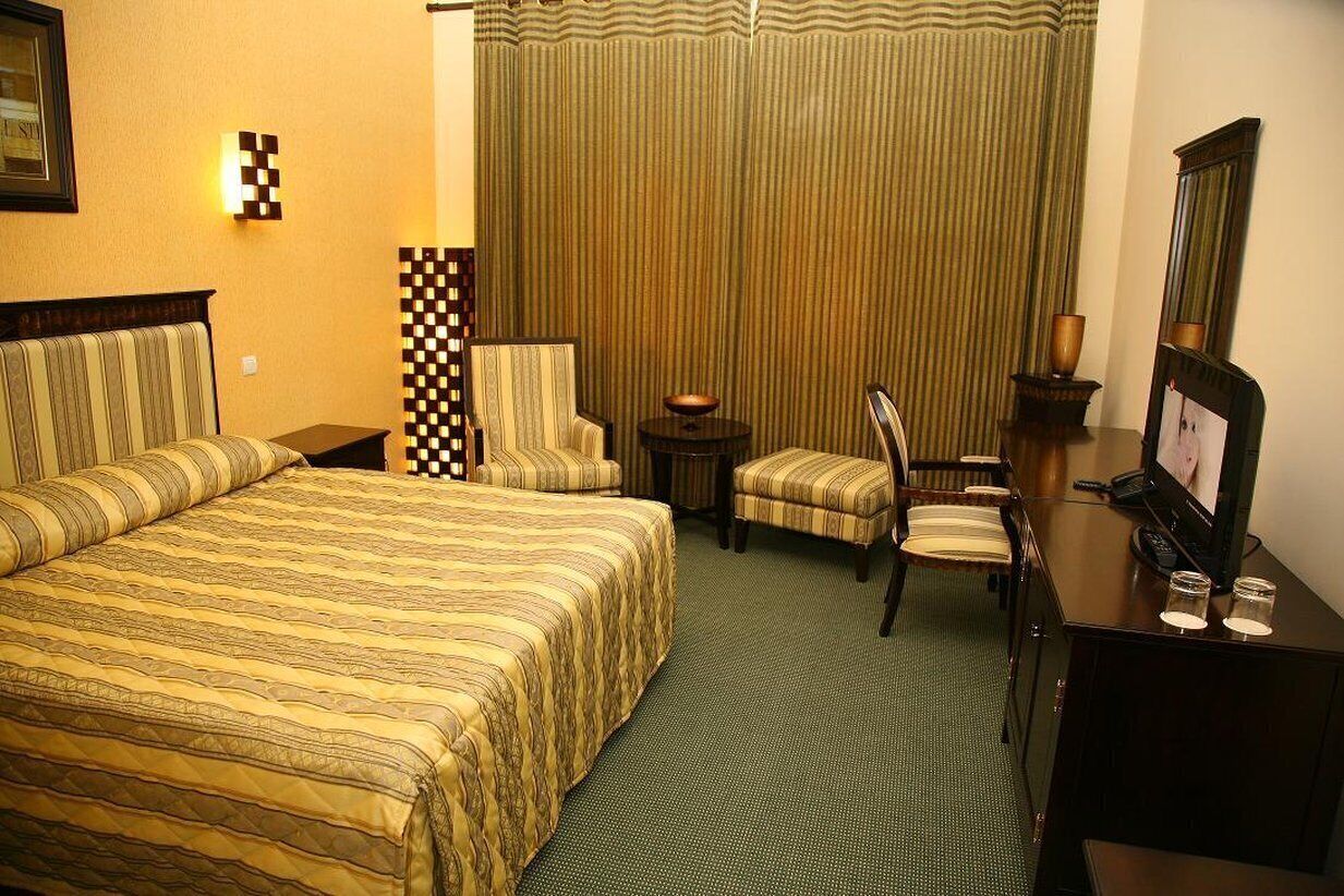 Een hotelkamer met een groot bed, twee fauteuils, een tafeltje, een bureau met een computer en een spiegel.