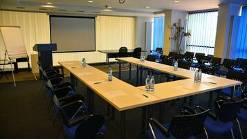 Un salón de conferencias con una larga mesa, sillas, una pantalla de proyector y una pizarra.