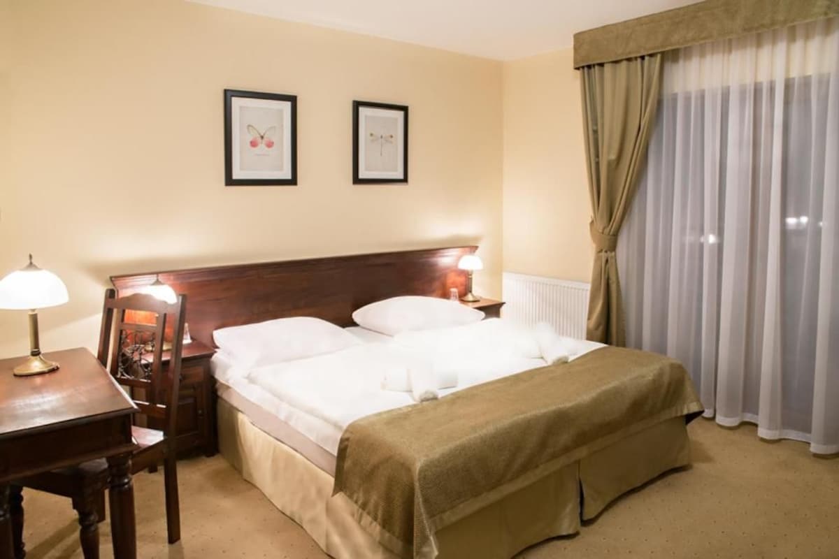 A hotel room with a bed, bedside lamps, a table, and two framed pictures on the wall.