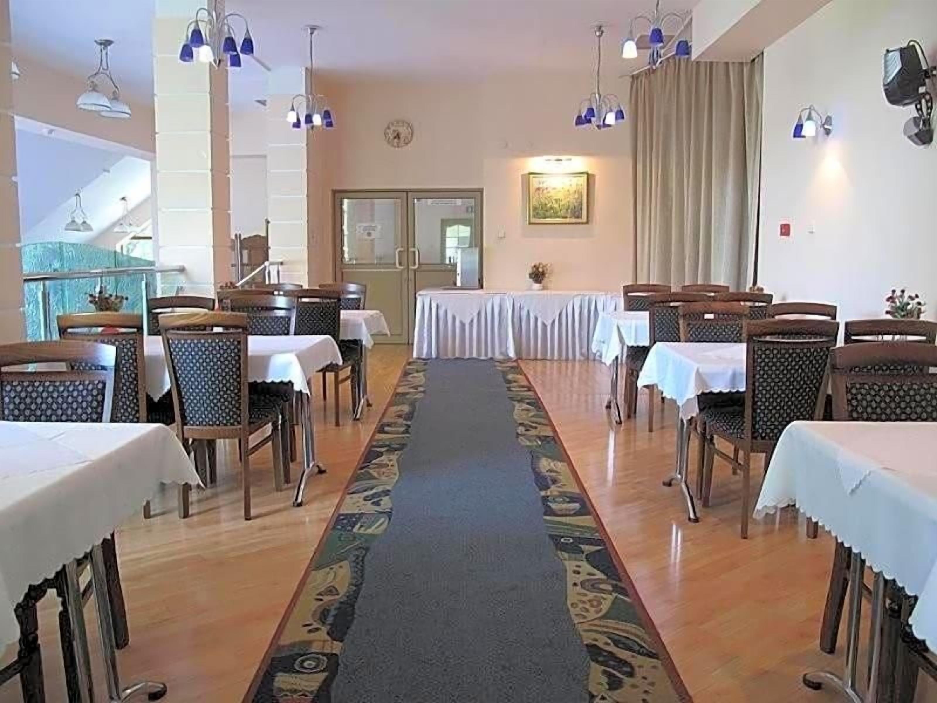Une salle à manger d’hôtel avec des tables et des chaises disposées en rangées, un tapis recouvrant le sol et des luminaires suspendus.