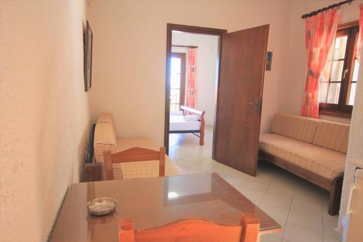 A room with a wooden table, a sofa, a bed, and a door leading to another room.