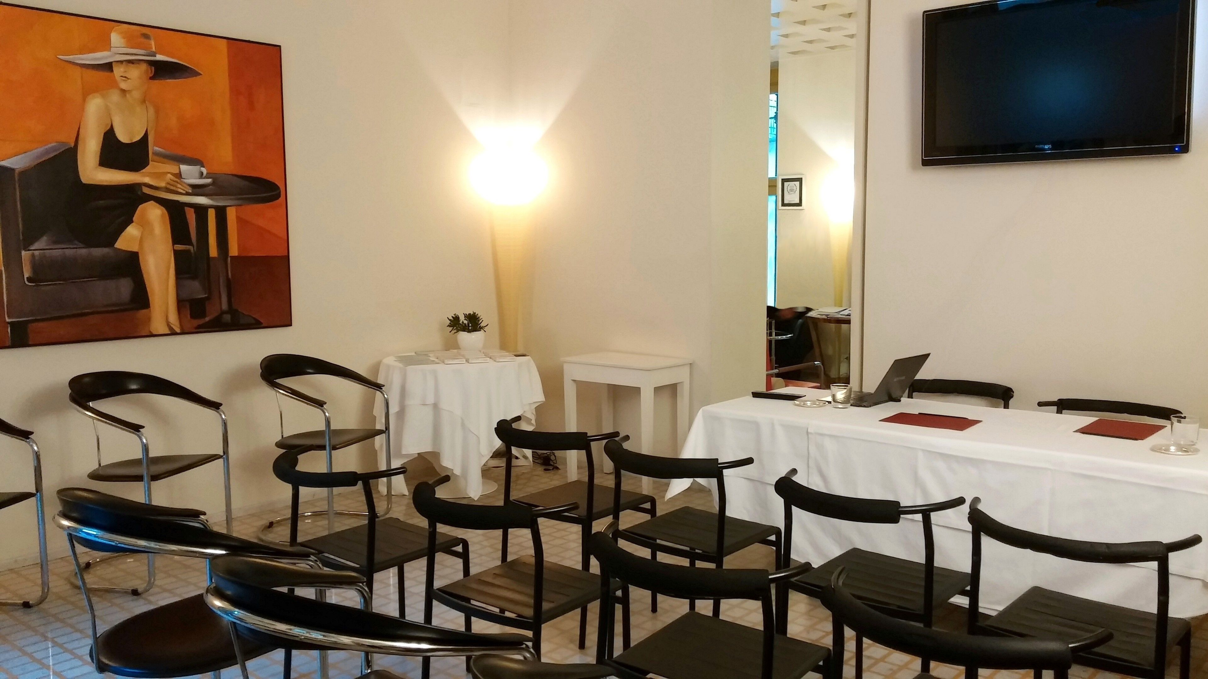 A conference room with a white table, black chairs, a TV mounted on the wall, and a painting on the wall.