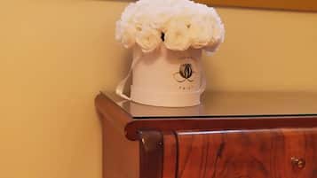 Una mesita de noche de madera con un jarrón blanco con flores blancas, un libro y otro libro rojo en una estantería.