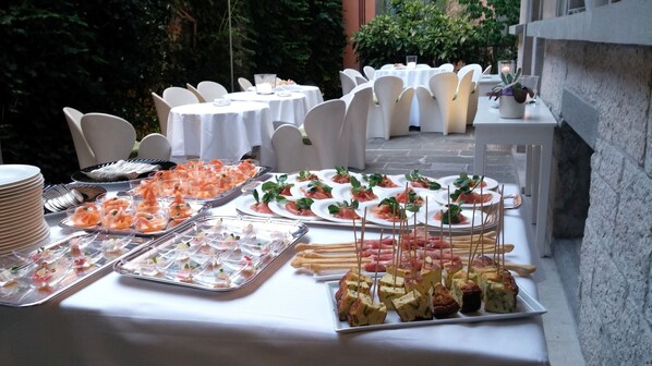 A buffet table with various food items, including shrimp, salads, and appetizers, set up outdoors with white tablecloths and chairs.