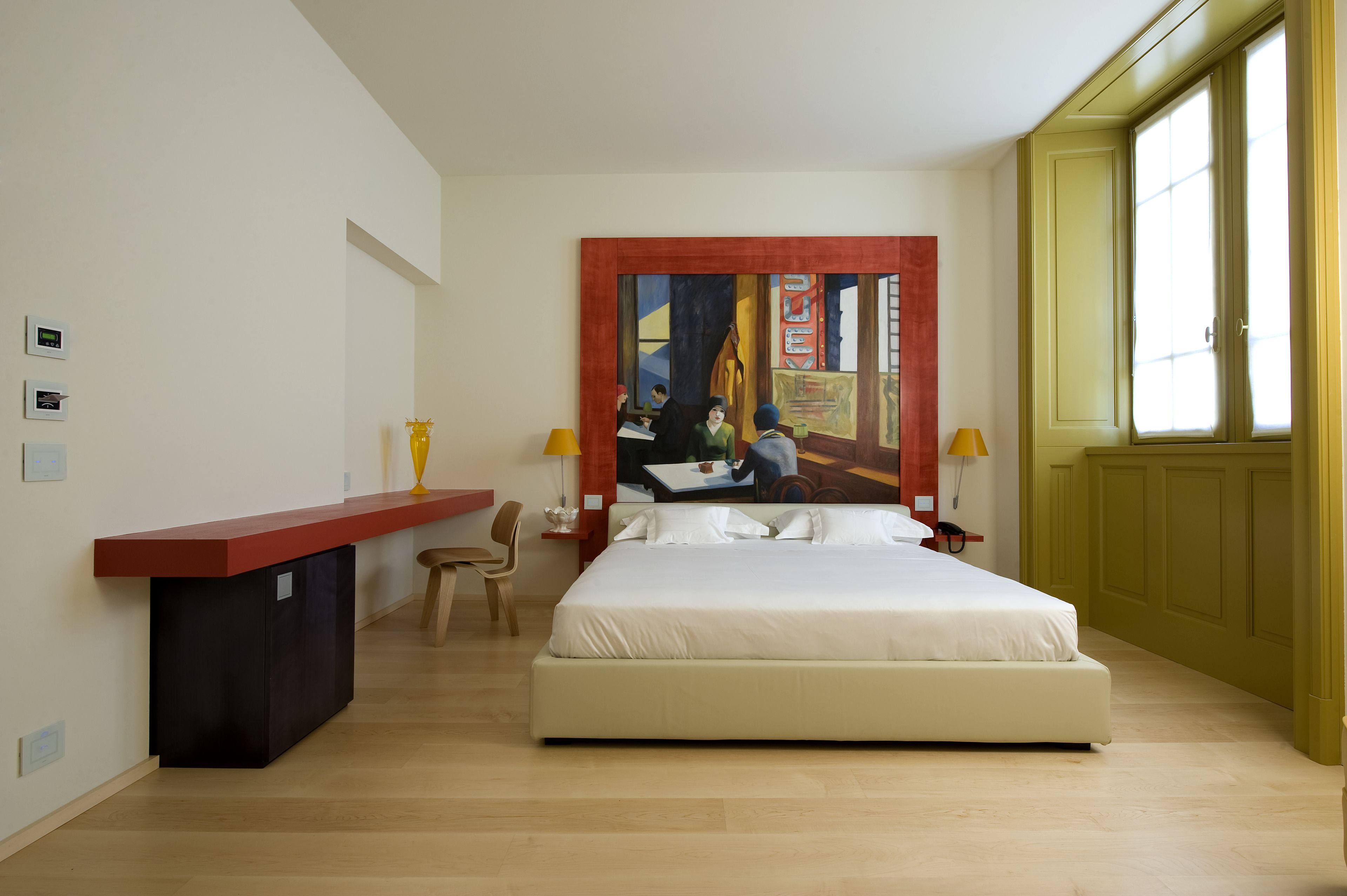 A hotel room with a large bed, a desk with a chair, a painting on the wall, and a window with yellow blinds.