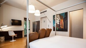 A modern hotel room with a large bed, a desk with a chair, a television, and artwork on the walls.