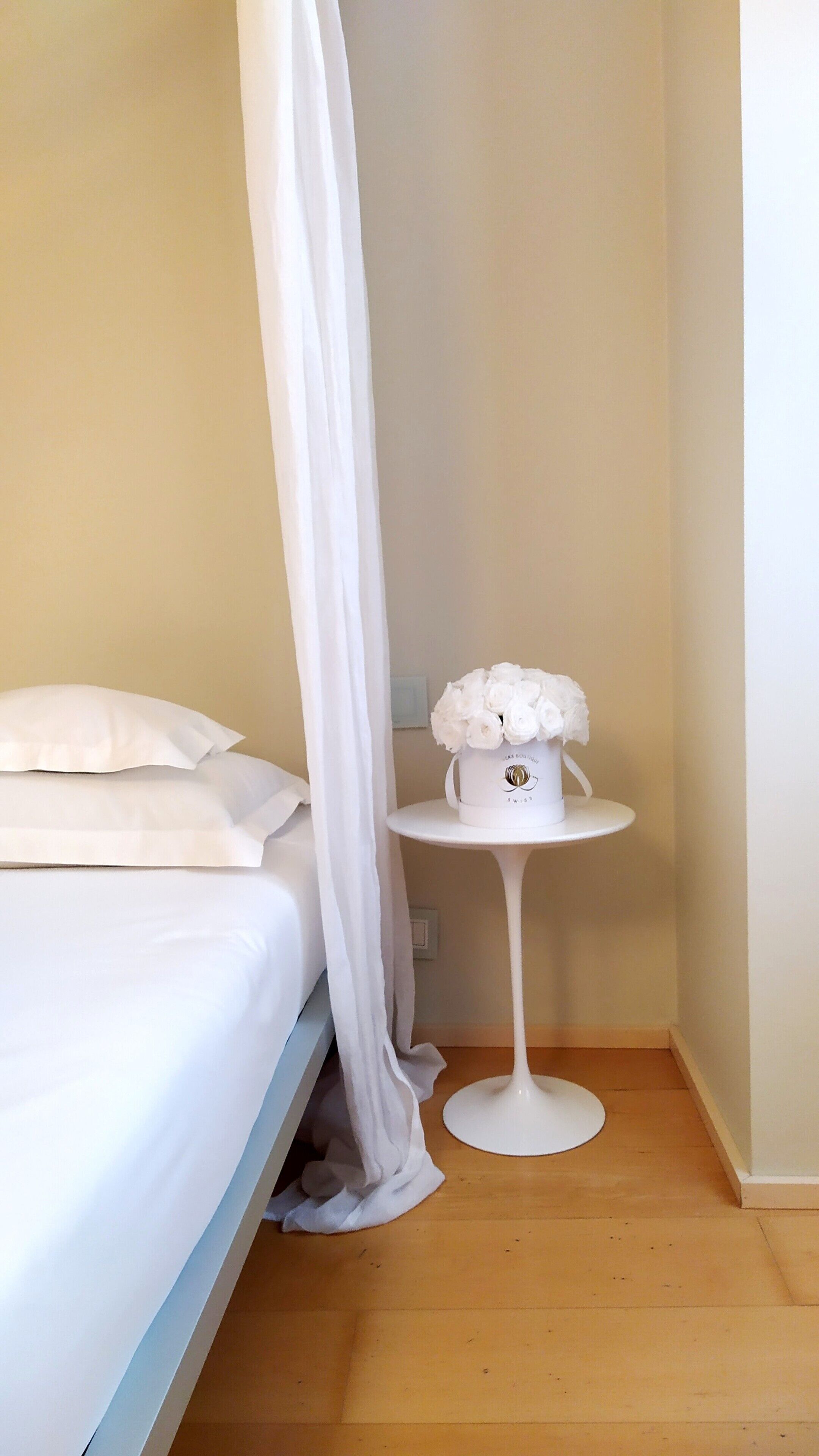 A bedroom with a bed, a white bedside table, and a white vase with flowers.