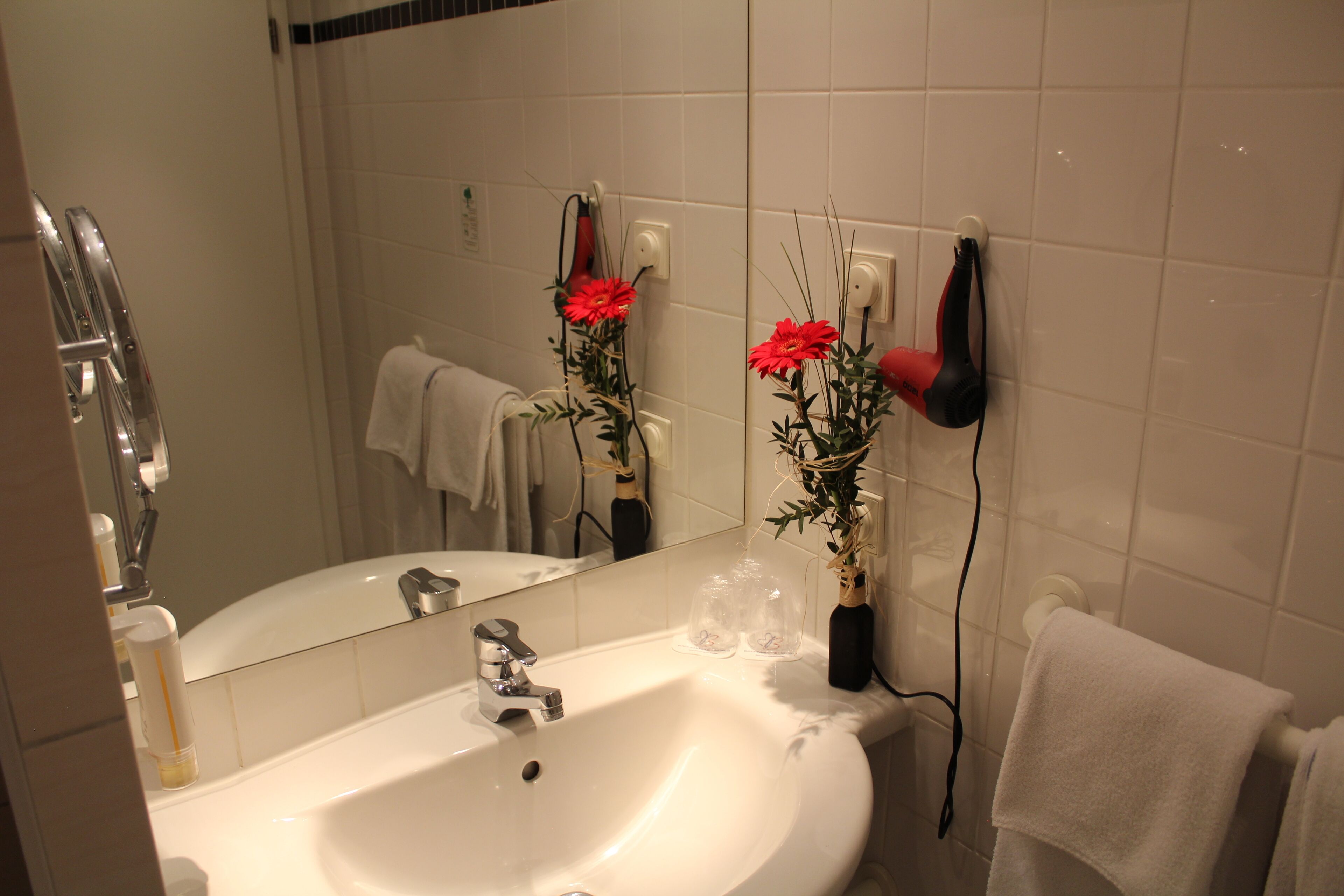 A bathroom with a sink, mirror, towel rack, and a hairdryer on the wall.