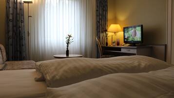 Ett hotellrum med två sängar, en tv, en lampa och en vas med blommor.