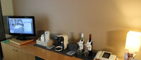 Mostrador de recepción de hotel con monitor de computadora, teléfono, botellas de vino y cafetera.