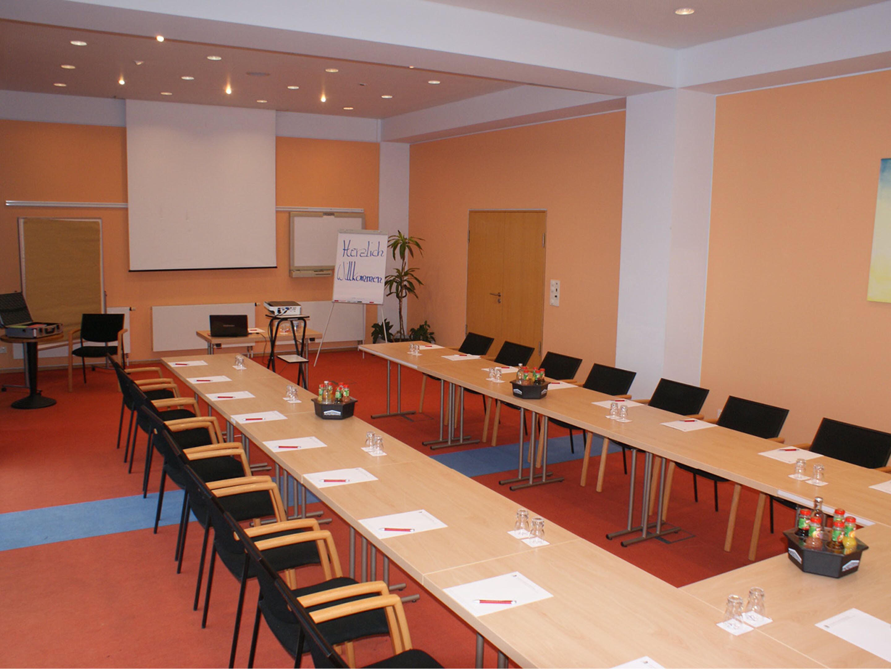 Een vergaderruimte met een lange tafel, stoelen, een whiteboard en een projectiescherm.