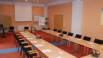 A conference room with a long table, chairs, a whiteboard, and a projector screen.