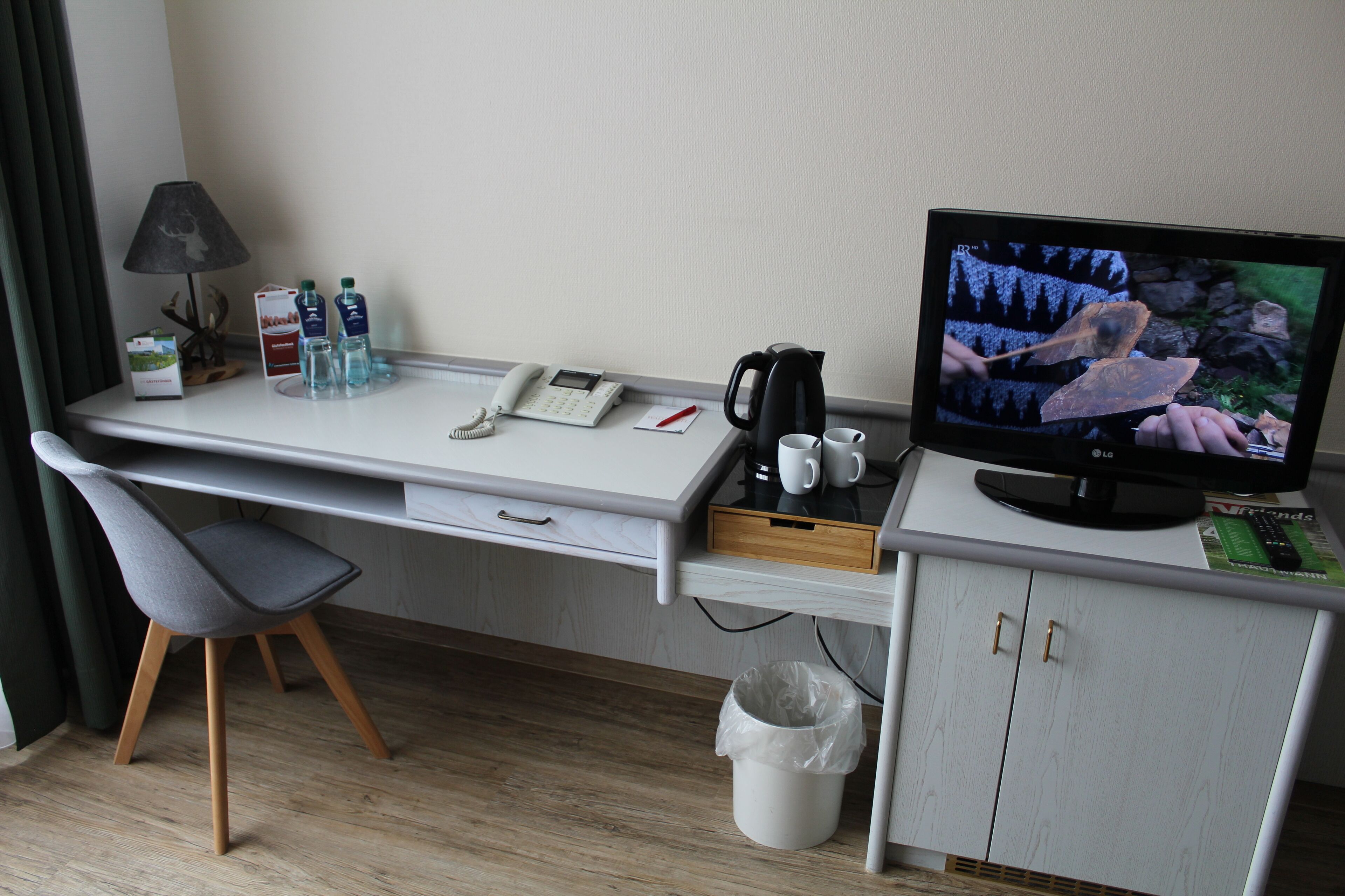 Quarto de hotel com escrivaninha, cadeira, televisão, telefone e diversos serviços.