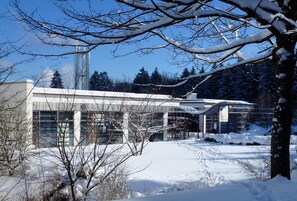 A modern building with a glass facade, surrounded by snow-covered trees and a clear sky.