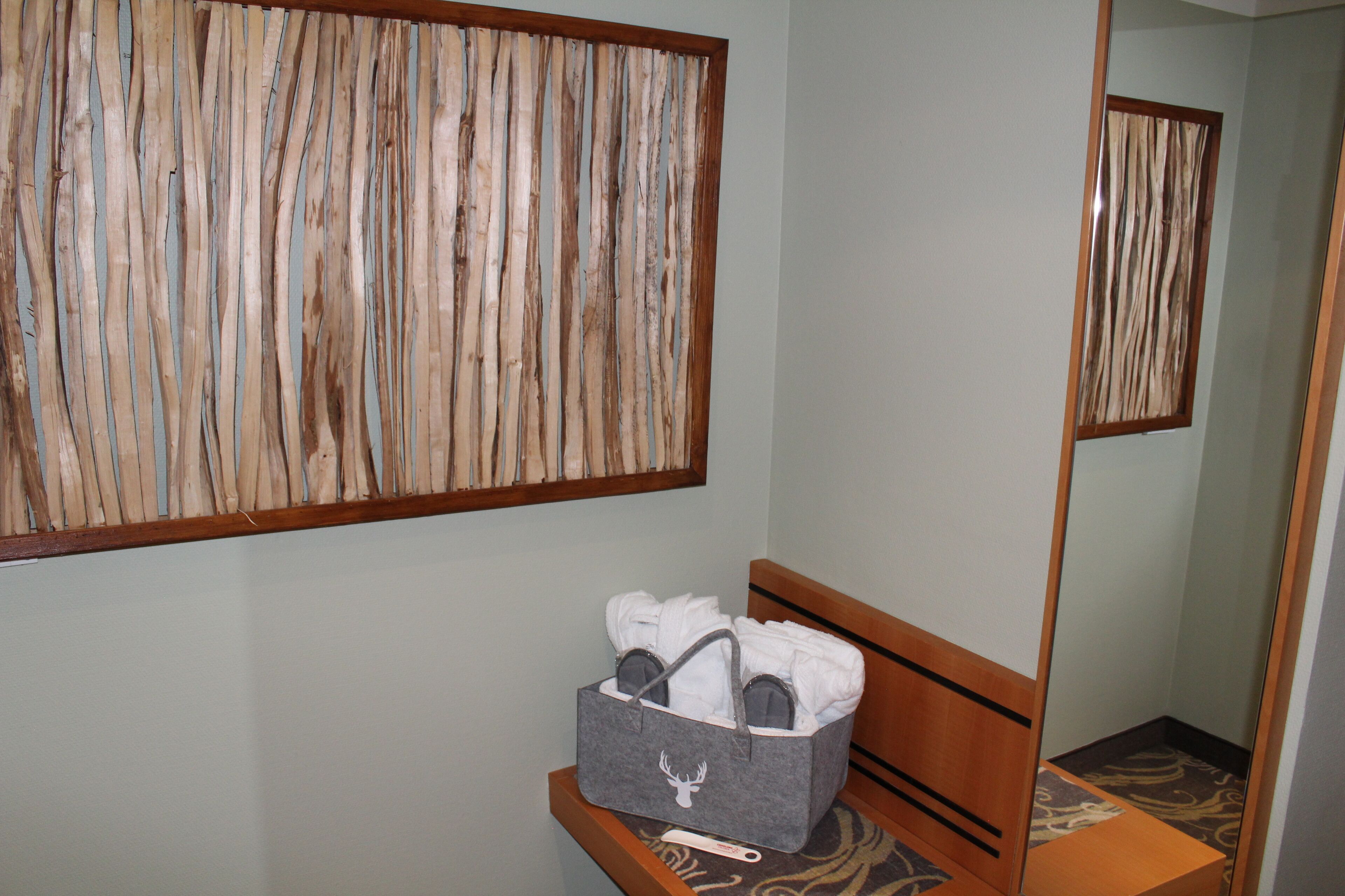 A bathroom with a wooden bench, a gray storage basket with towels, and a mirror on the wall.