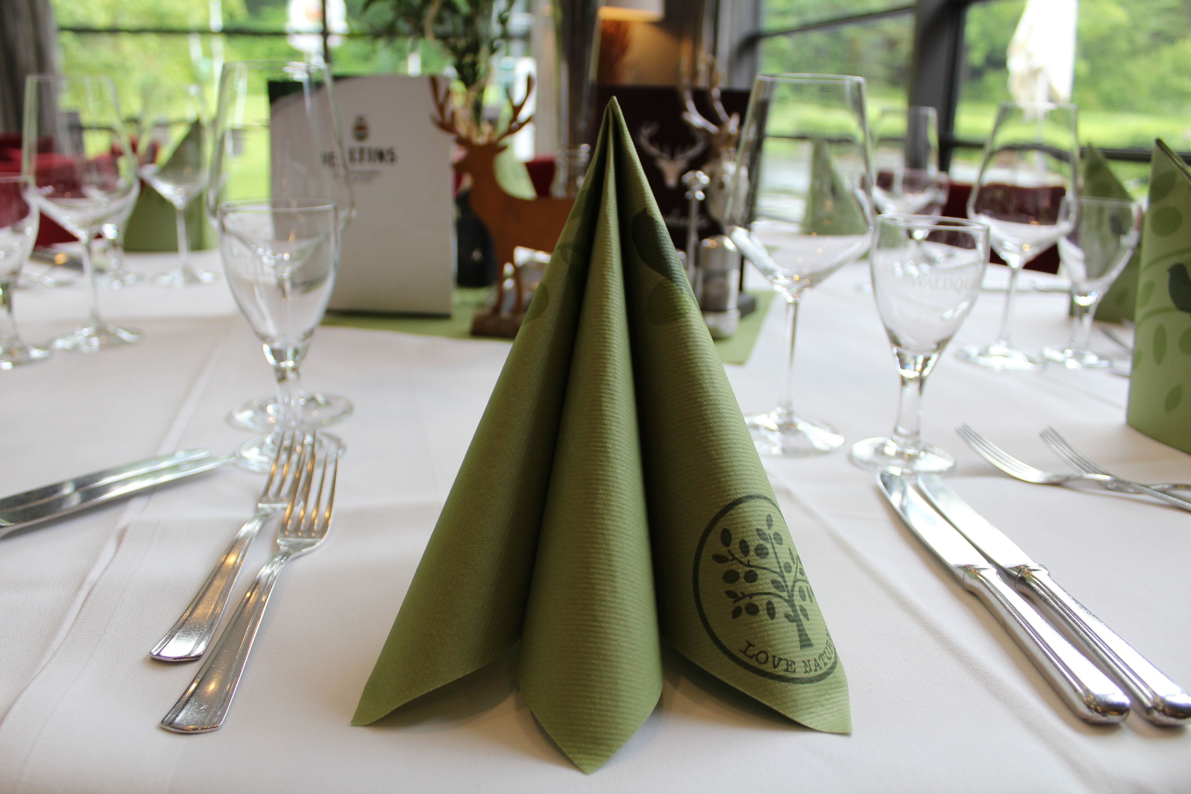A table set for a meal with a green napkin, silverware, and wine glasses.
