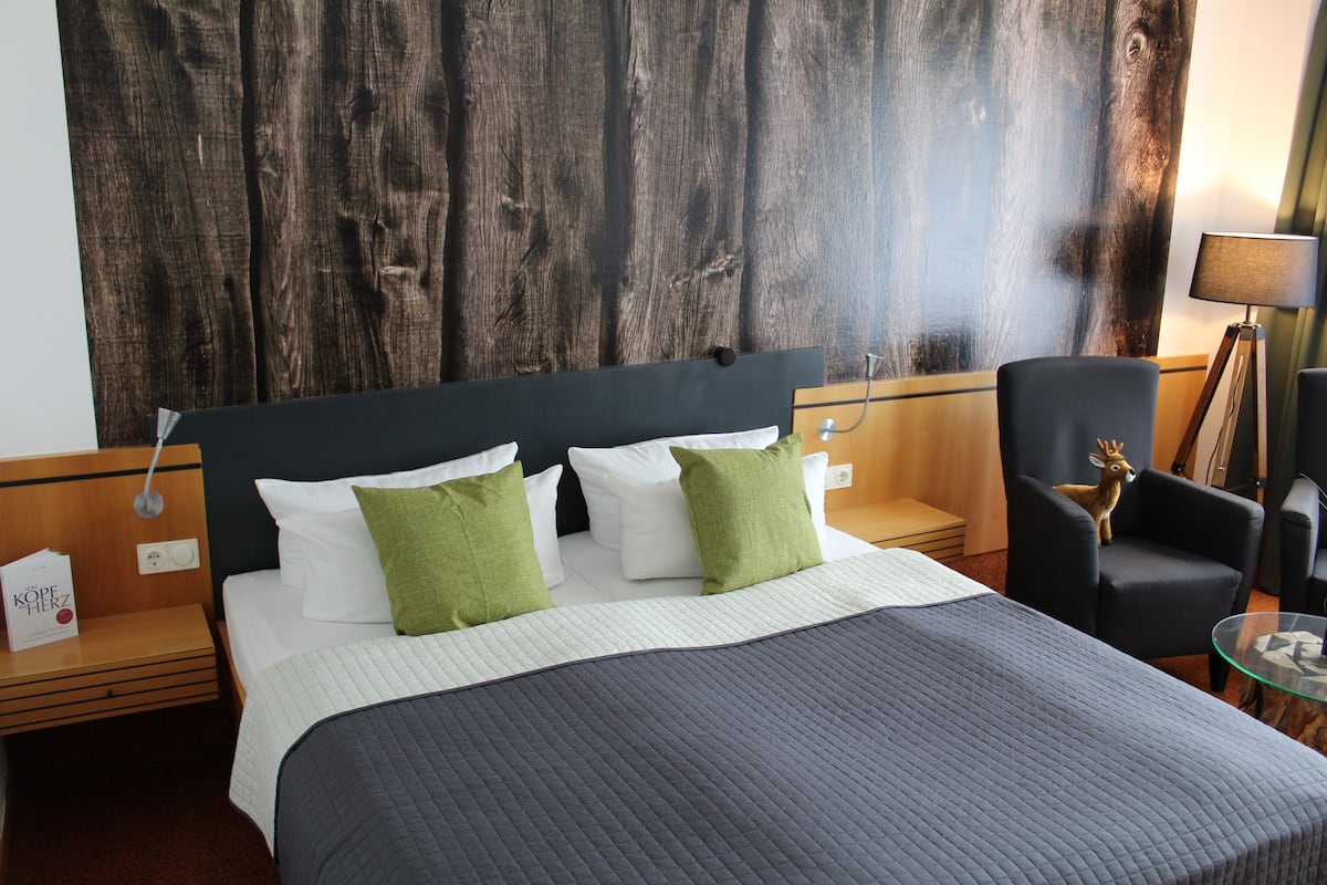 A hotel room with a bed, a nightstand, a lamp, a chair, and a large wooden wall.