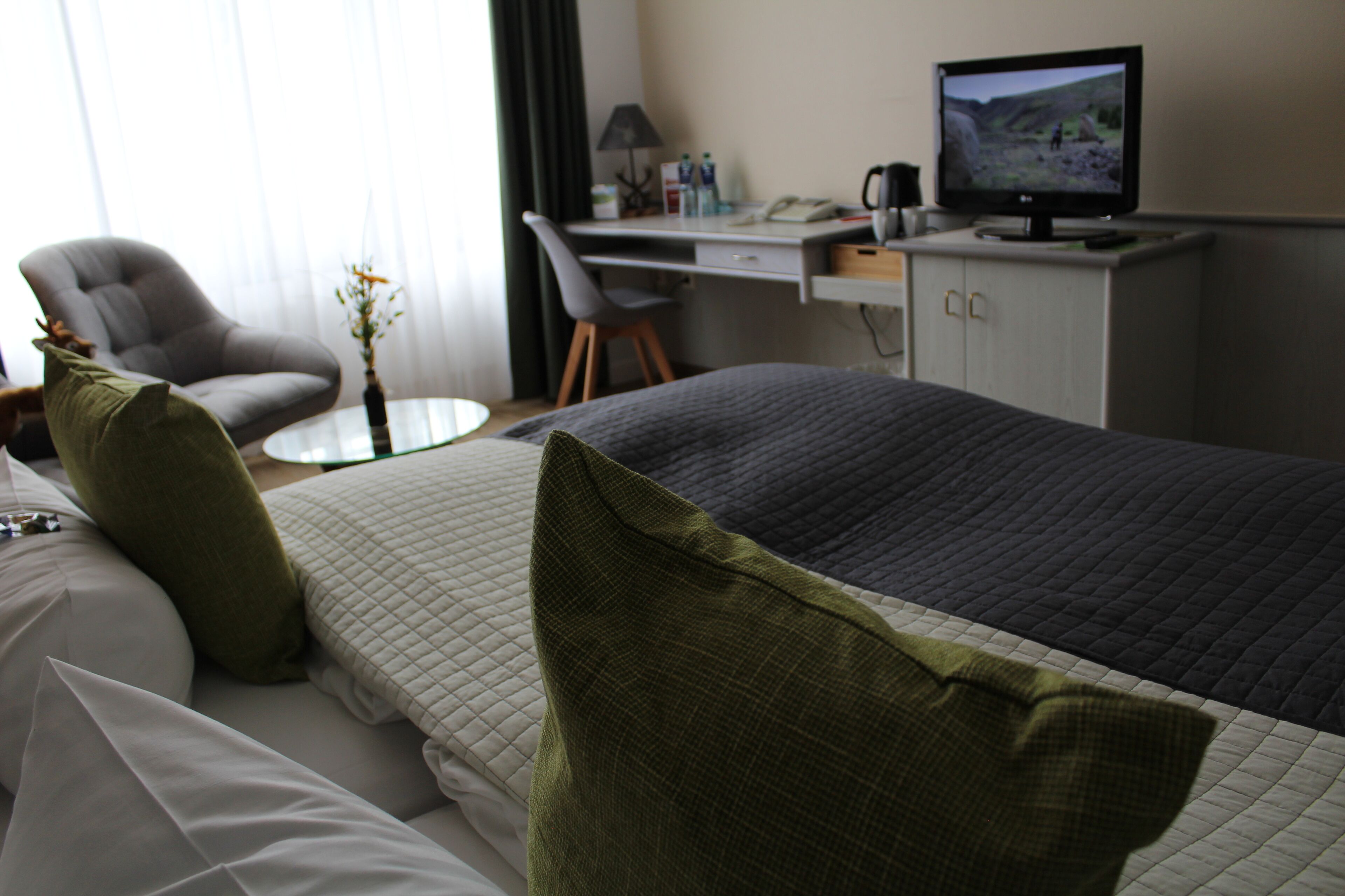 Ein Hotelzimmer mit einem Bett, einem Schreibtisch mit Computer, einem Sessel und einem Fernseher.