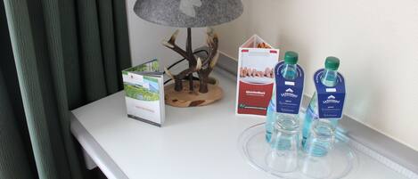 Una mesa con una lámpara, un folleto, una planta decorativa y dos botellas de agua.