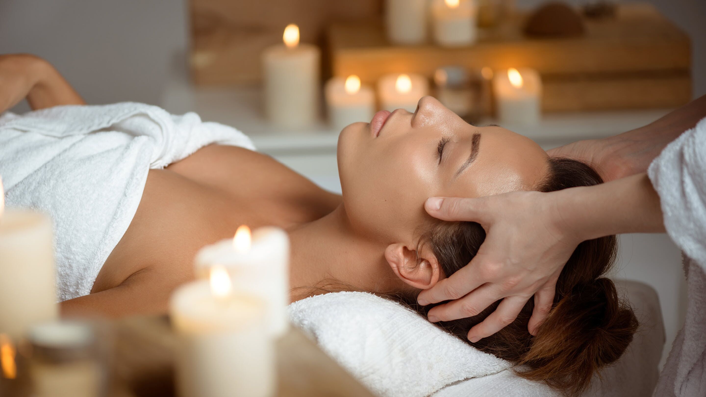 A person receiving a massage in a spa setting with candles and a wooden massage table.