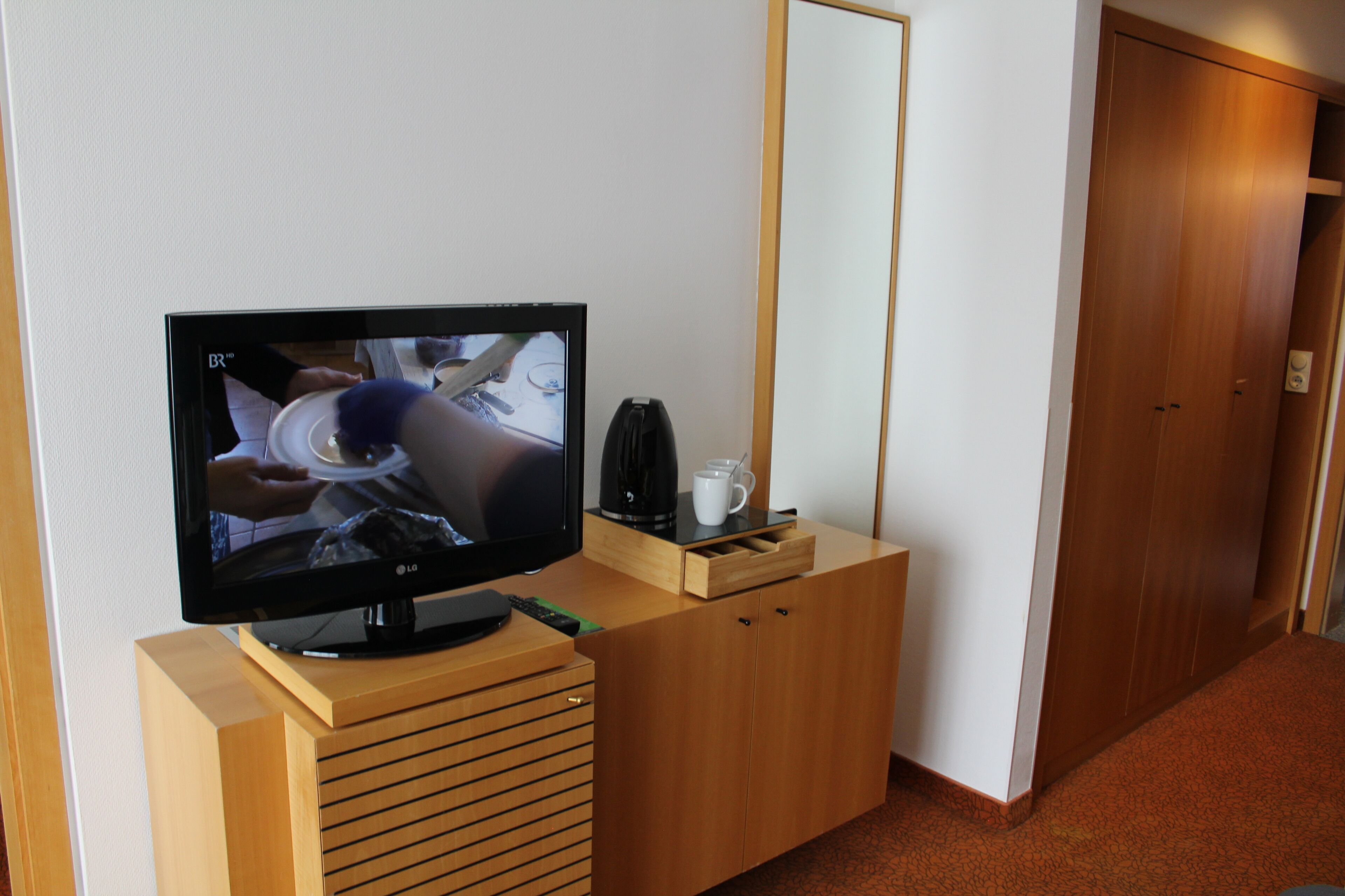 A television on a wooden stand, a coffee maker, and a cup on the stand.