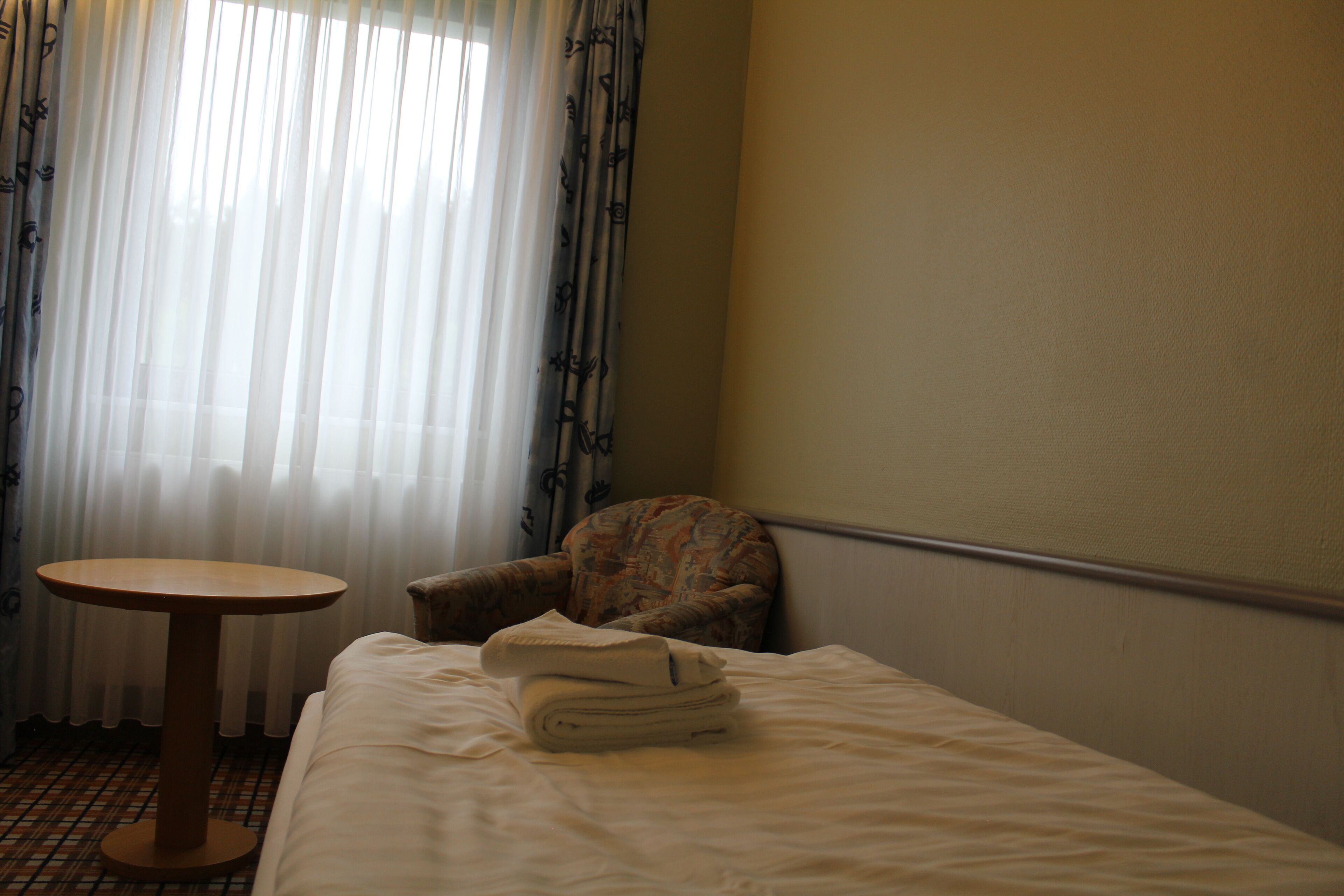 A hotel room with a bed, a small round table, and a chair.