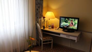 A hotel room with a television, a desk, a chair, a lamp, and a vase with flowers.