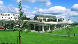 A modern building with a large glass facade, a green lawn, and a clear sky. - Hotel Rennsteig (Masserberg)