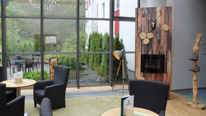 A modern interior with large windows, a wooden wall with antlers, and a shoe rack. - Hotel Rennsteig (Masserberg)