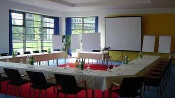 Ett konferensrum med ett långt bord, stolar, en projektorduk och fönster med blå gardiner.